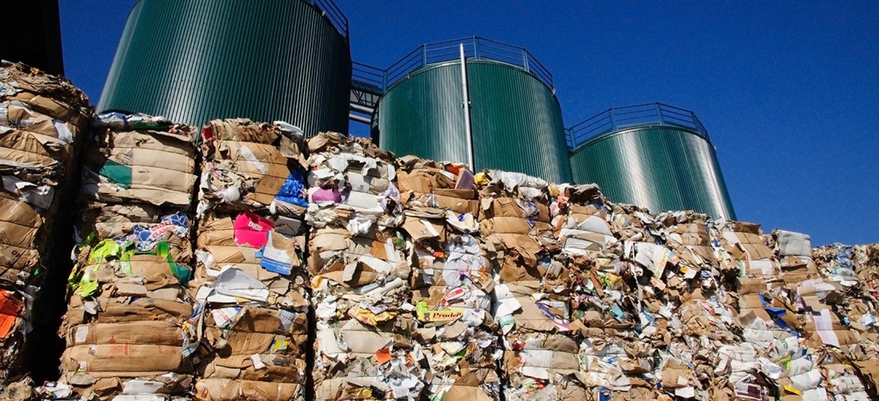 Piles of compressed trash in front of three silos.