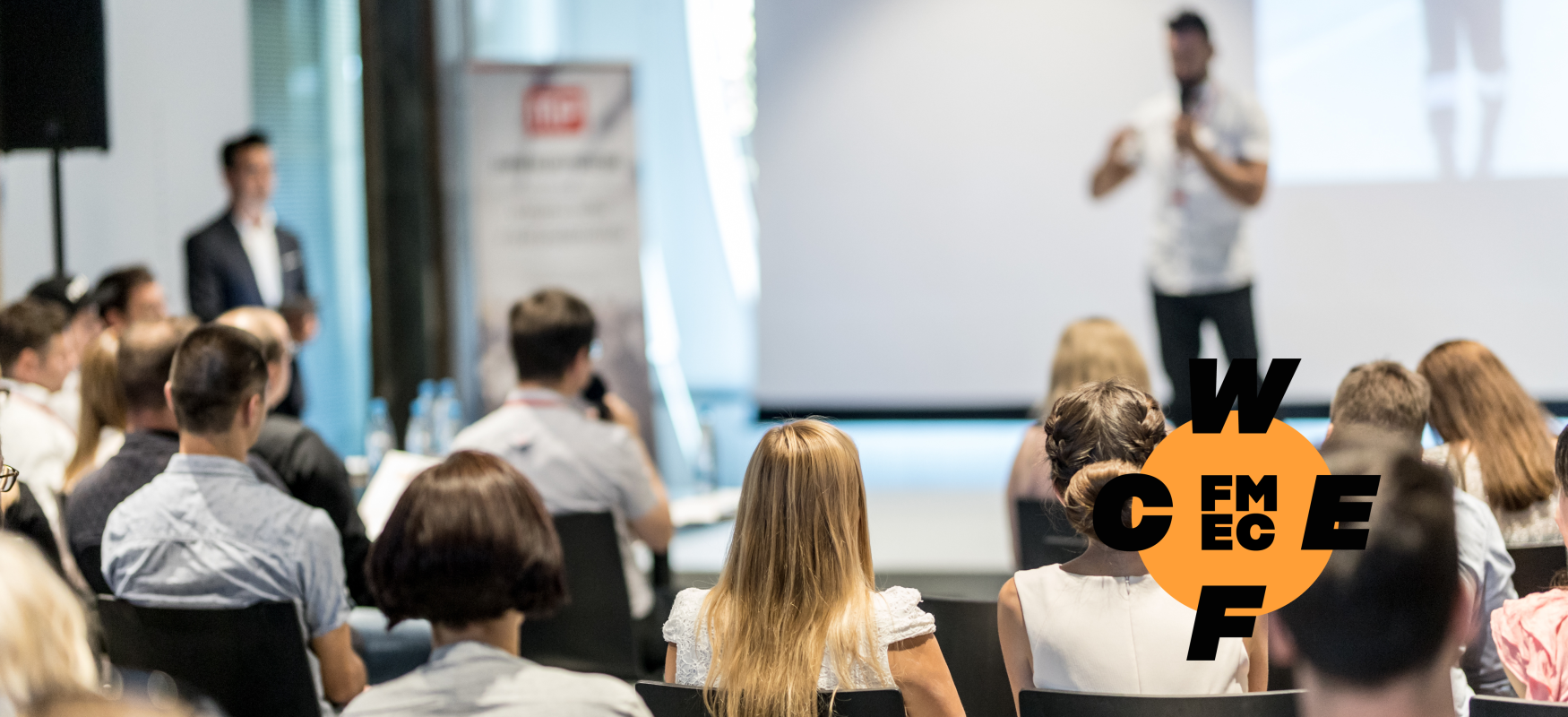 Man standing one stage pitching his idea to a seated audience.