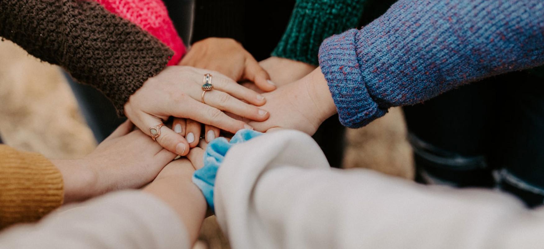Team of people with coloured knit sweaters putting their hands together.