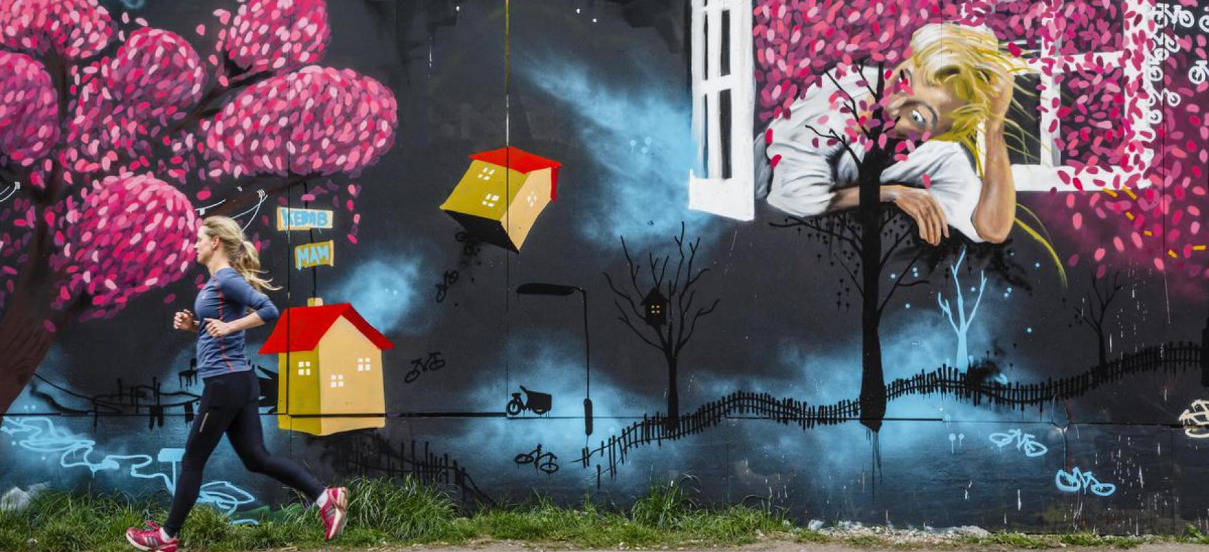 Woman running past graffiti wall.