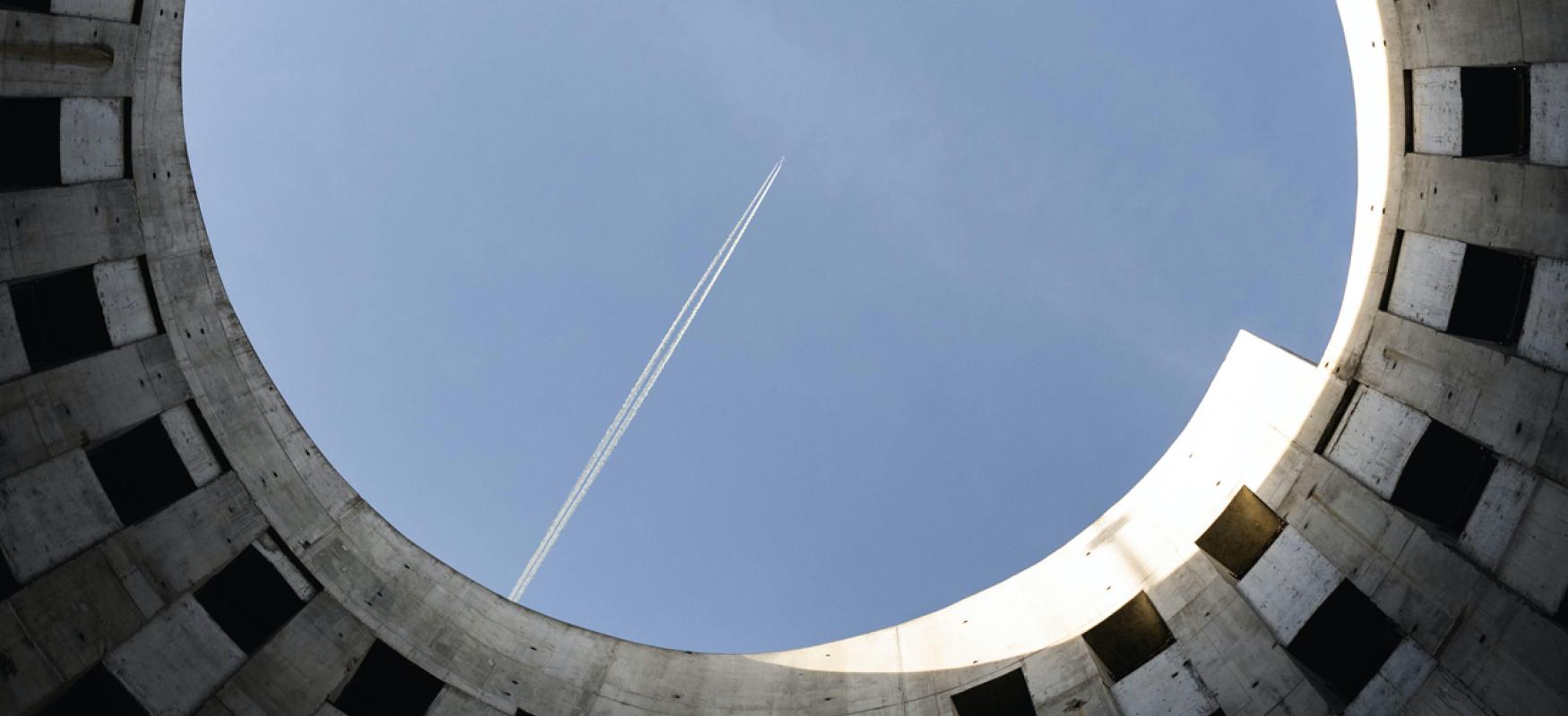  photography taken stright upward of brown concrete building under blue sky and a plane. Photo by Ben Krb on Unsplash