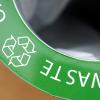 Closup of a green sign saying "Waste" and with a classic recycling logo.