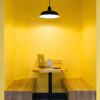 Booth with two benches and a table with a laptop on top. Yellow wall.
