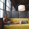 Woman sitting in a sofa with a computer and working. Large lamp hanging over the sofa.