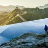 Split image with the Great Wall of China in sunrise on the top and a man standing overlooking a fjord on the bottom.