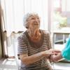 Elderly woman on a chair holding the hands of a nurse.