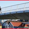 Man cyckling over a bridge with wooden houses in the background